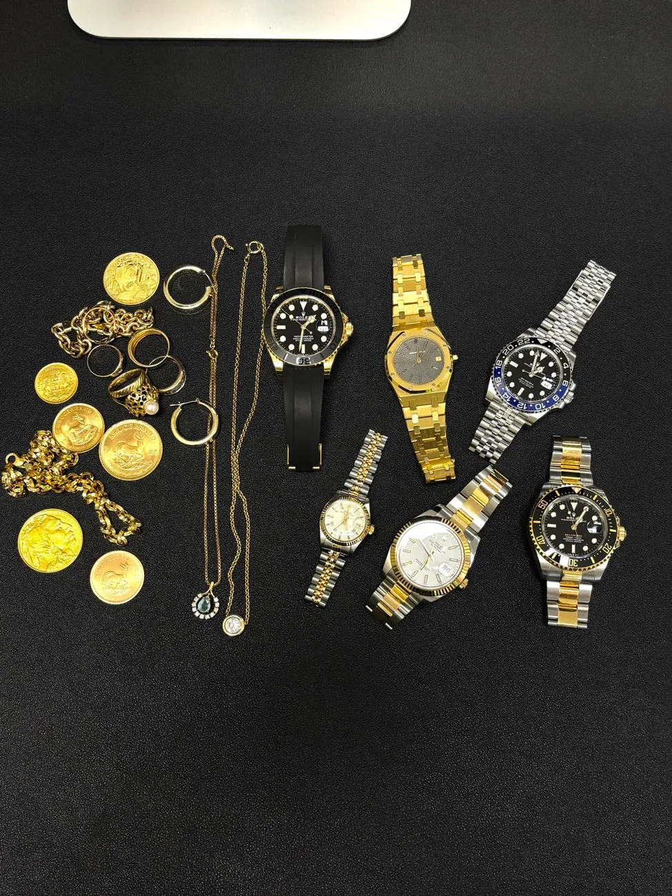 Rolex-Uhren, Goldmünzen und Ketten auf einem Tisch