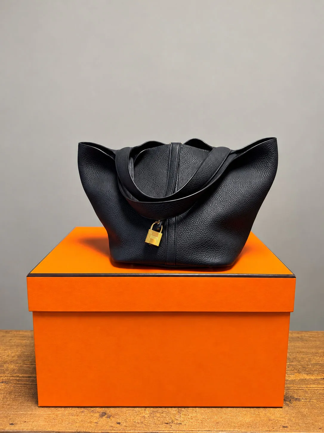 Schwarze Ledertasche mit goldenem Schloss auf einer orangefarbenen Geschenkbox